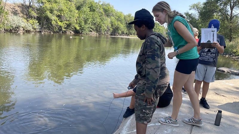 students testing water temperature at the river